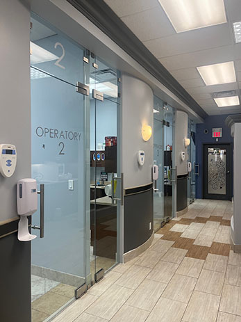 The image shows an interior view of a building with a modern lobby featuring glass walls, a tiled floor, and a reception area with signage for Operators and a door marked with the number 2.