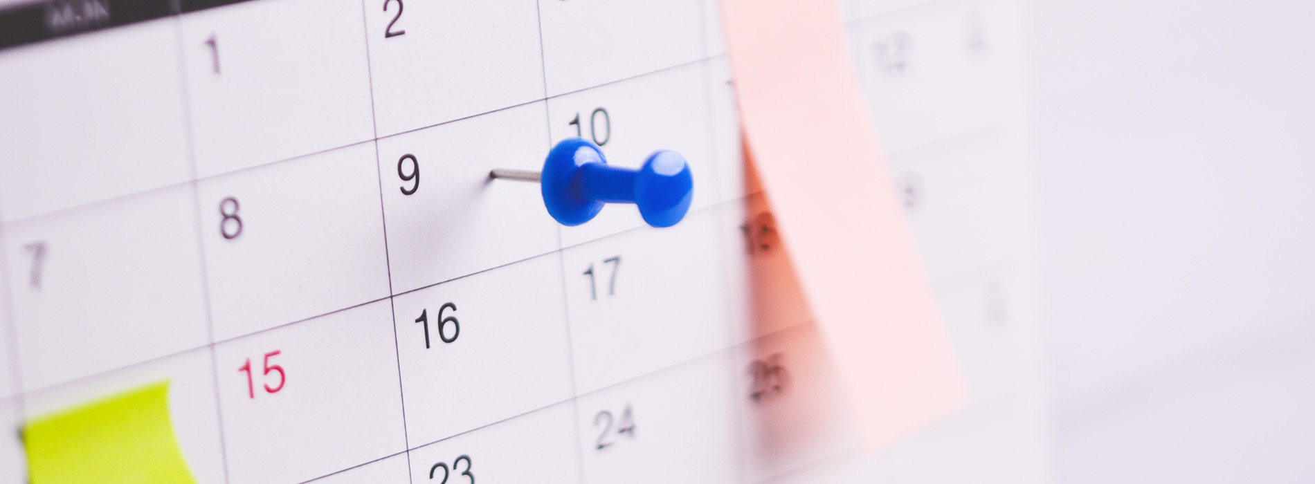 The image shows a close-up view of a calendar with a pen pointing at a specific date, placed on a surface with a blurred background.