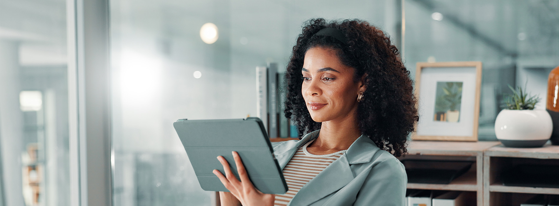 The image shows a person holding a tablet while standing indoors, possibly within an office setting, with a blurred background suggesting a professional environment.