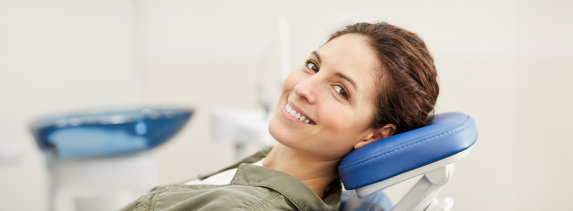 A woman sitting in a dental chair with her head resting on a support, smiling at the camera.