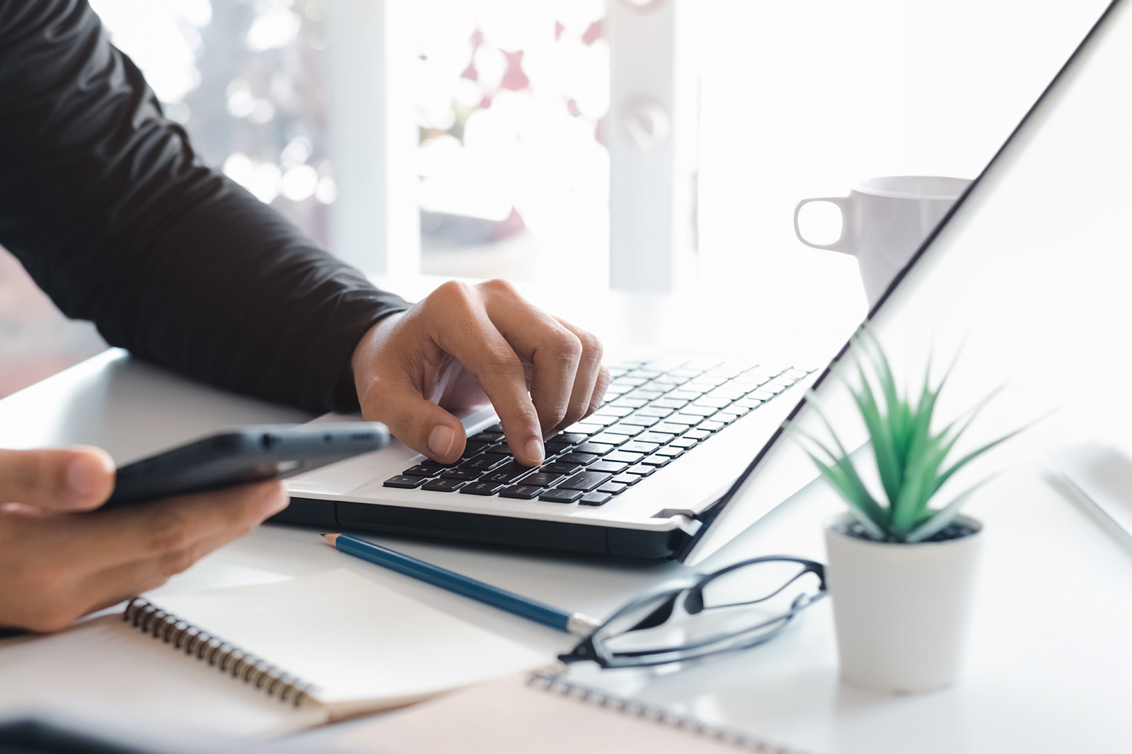 A person s hands working on a laptop computer at a desk with a cup of coffee nearby.