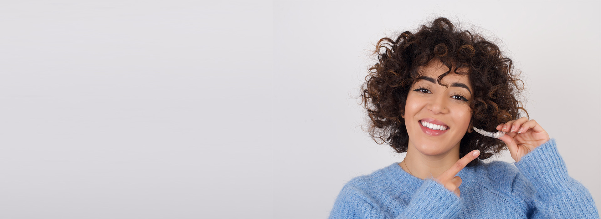 A woman with curly hair smiling while holding a toothbrush.