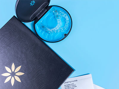 An image featuring two closed cosmetic product containers with an open lid on one side, placed against a blue background, and a box with a floral pattern nearby.