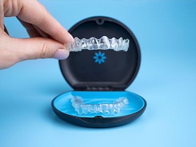 An image showing a pair of clear braces with a blue case opened beside them, revealing a single toothbrush inside.