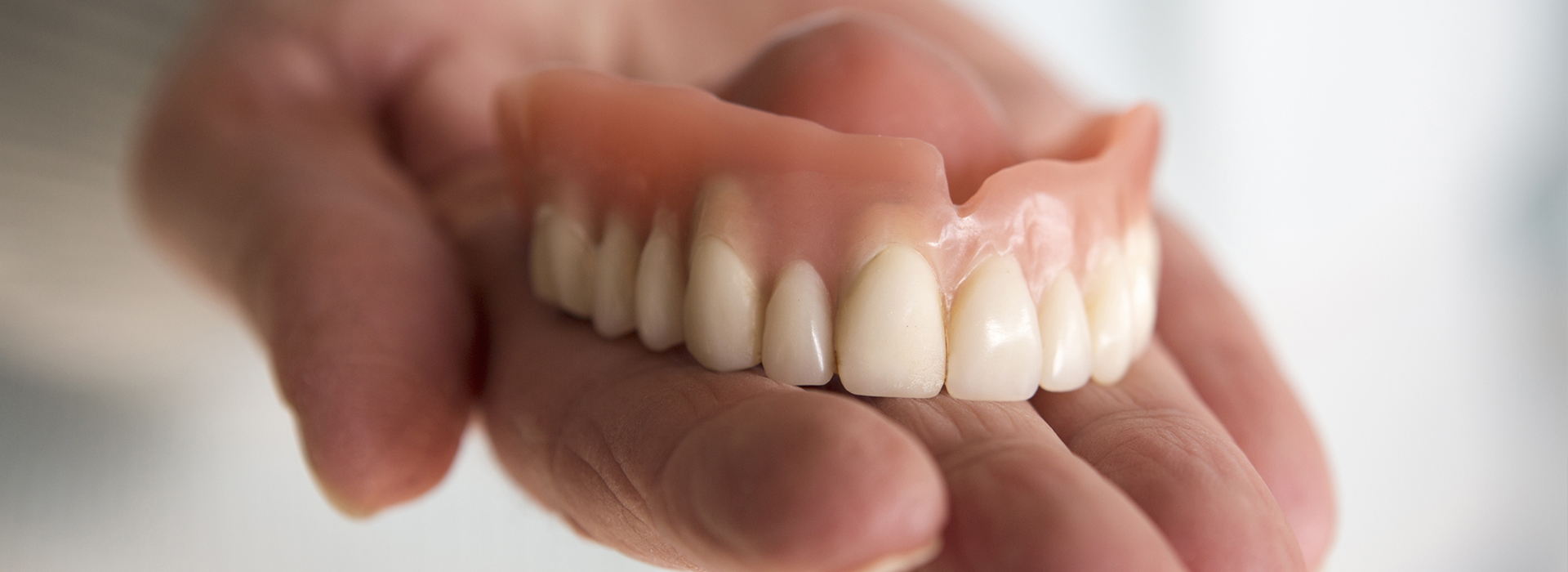 A person s hand holding a set of dentures with an open mouth displaying artificial teeth.