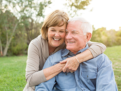 In the image, there are two elderly individuals sharing an affectionate moment  they are outdoors during daylight, with a clear sky above them, and appear to be enjoying each other s company.