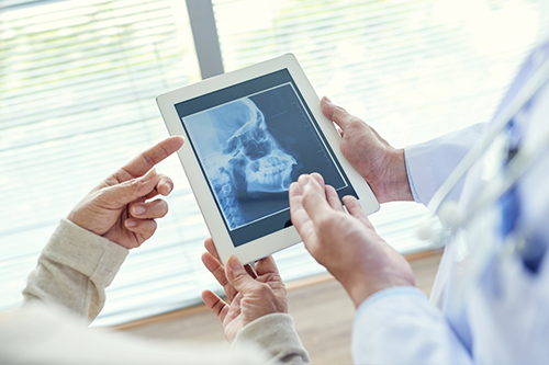 The image shows two people interacting with a tablet displaying an X-ray while standing in a medical setting, with one person holding a tablet and another pointing at it.