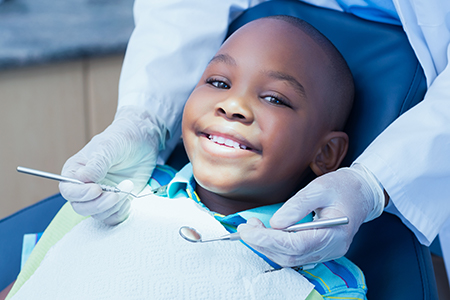 A young boy sitting in a dental chair with a smile on his face, receiving dental care from a dentist.