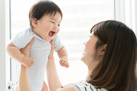 The image depicts a woman holding a baby with a joyful expression while looking at the camera.