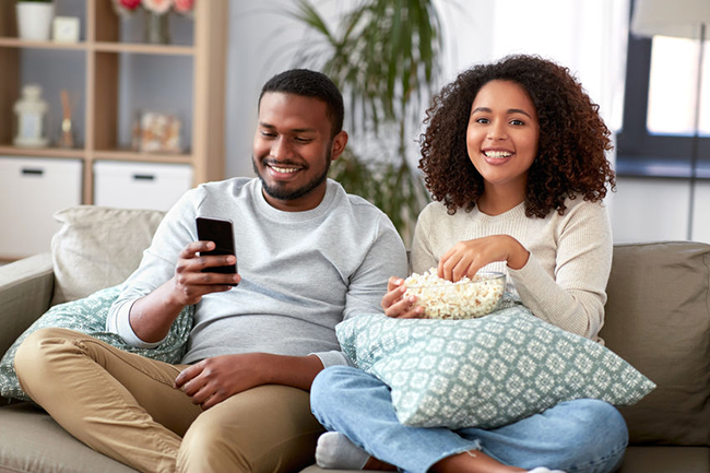 A couple sitting on a couch, sharing a moment together while watching something on their phone.