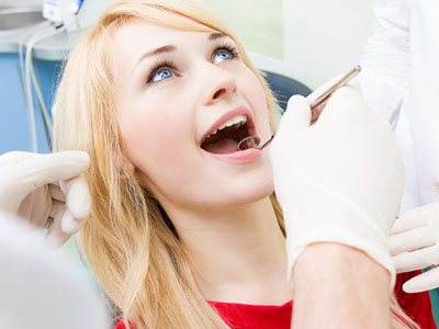 A woman receiving dental care with a dentist performing the procedure on her, set against a backdrop of medical equipment.