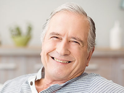 A man with gray hair, wearing a blue shirt, sitting comfortably with his eyes closed and smiling, appearing relaxed and content.
