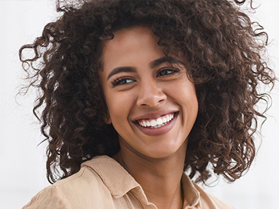 The image features a young woman with curly hair smiling at the camera, wearing a beige top.